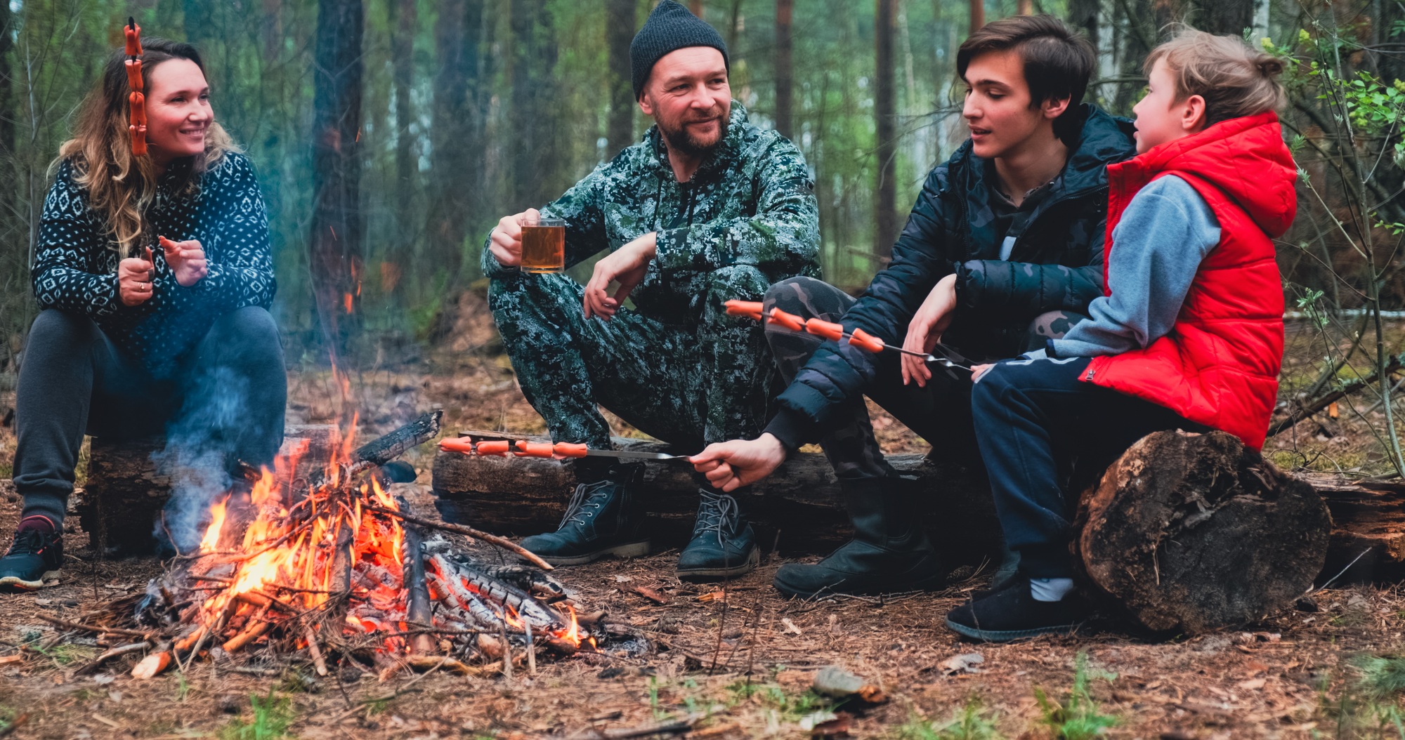 Family sits around a campfire on a summer evening.