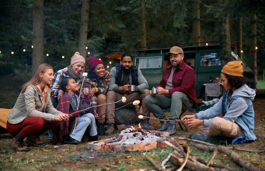 Multiracial families roasting marshmallows while gathering around campfire in the woods.