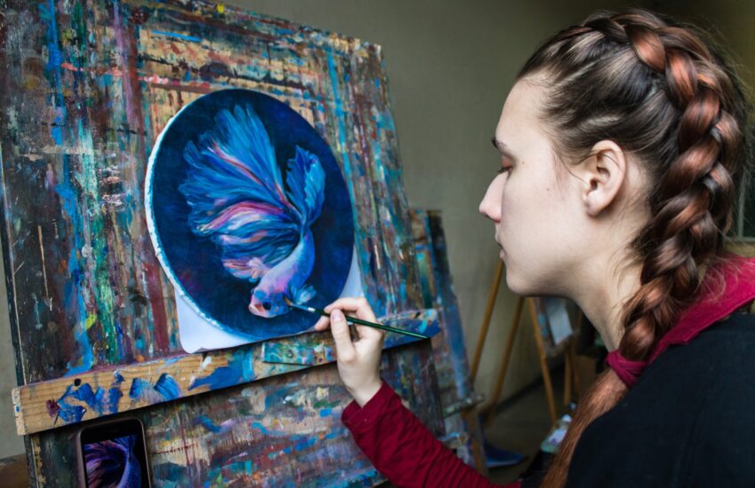 Portrait of young girl painting in the studio with oil paints a picture of big fish
