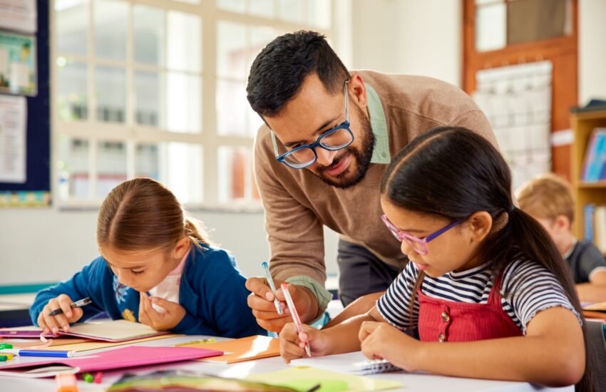 Teacher helping schoolchildren during lesson in classroom